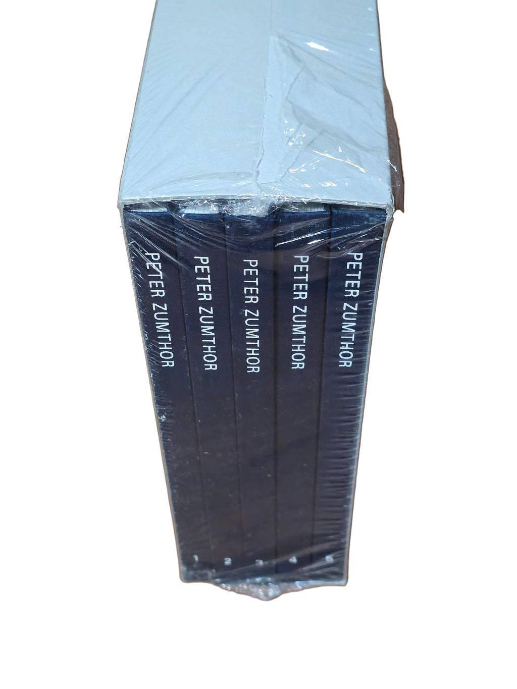 Stack of books titled 'Peter Zumthor' wrapped in plastic on a wooden surface